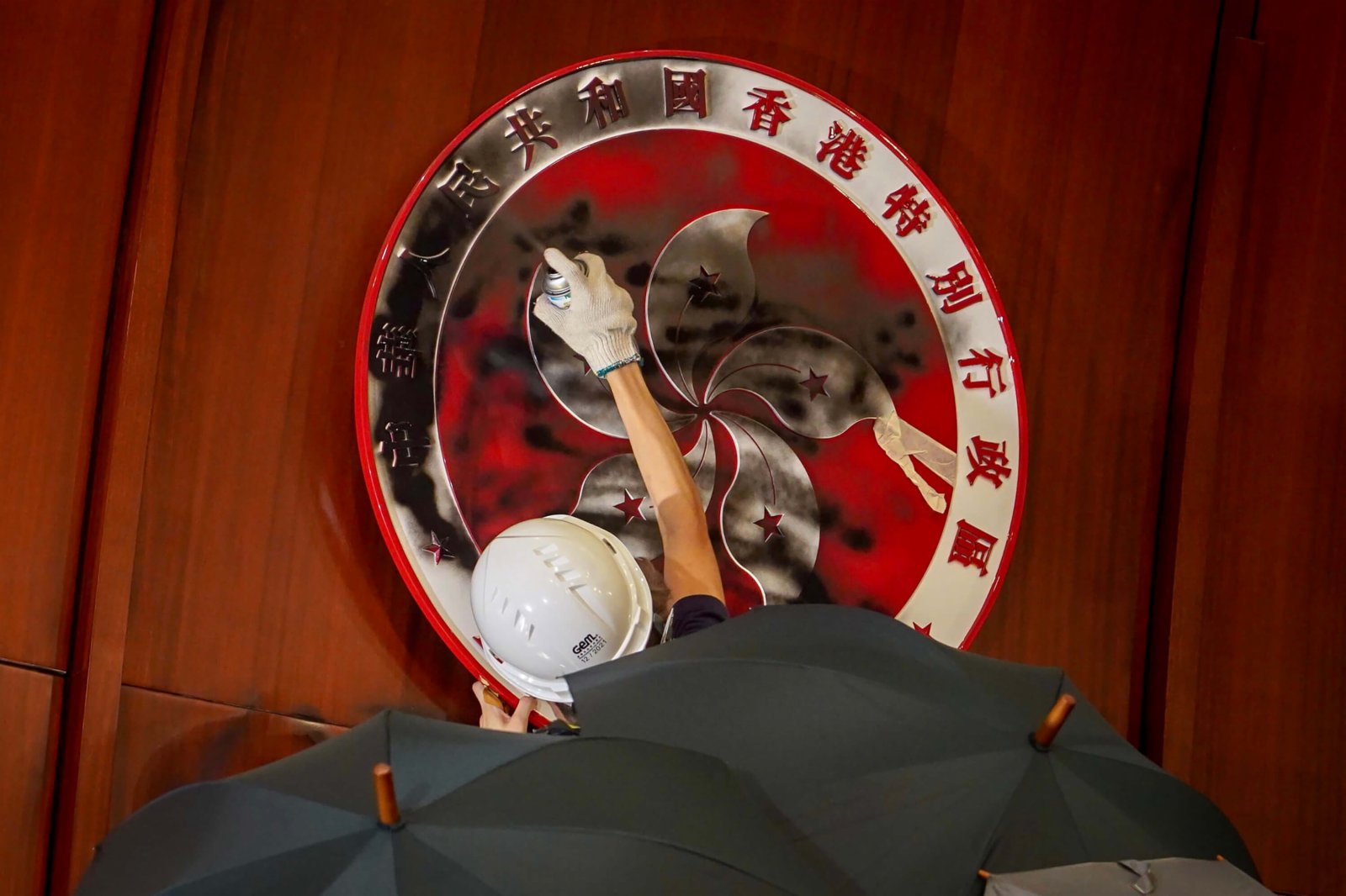 2019年7月1日，「民陣」舉行第五次示威遊行，反對《逃犯條例》修訂。大批香港示威者晚間撬開立法會鐵門後進一步佔領會議廳，一名示威者將會議廳內的特區政府區徽塗黑(「中央社」)