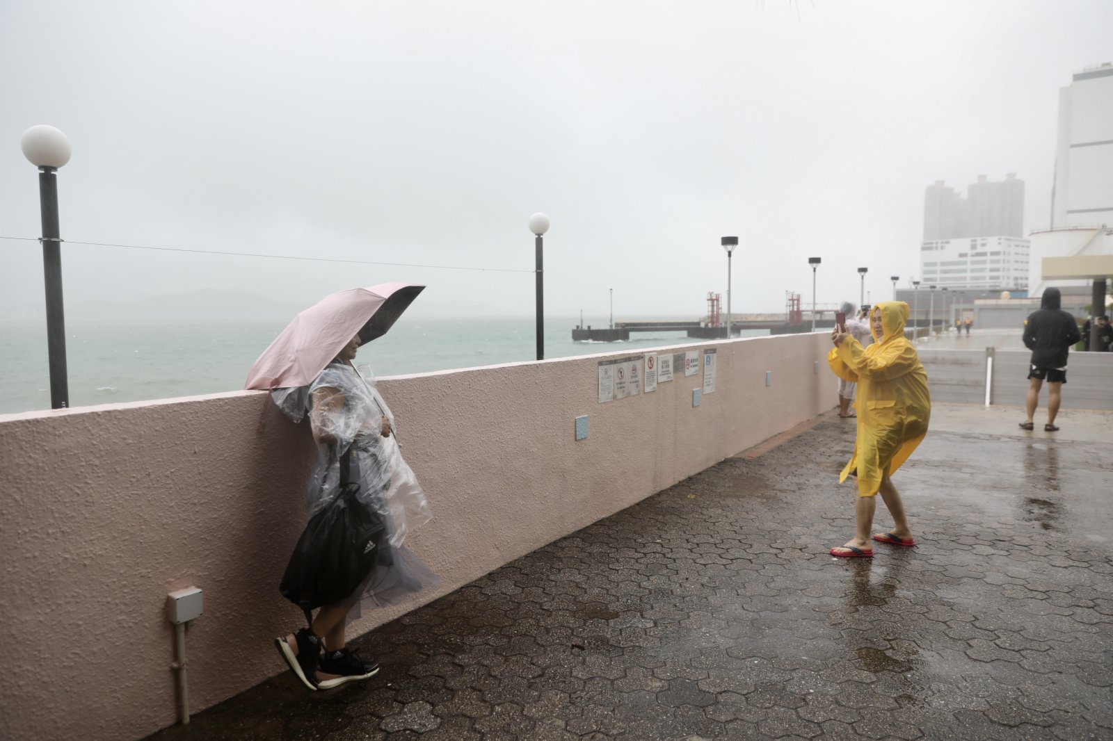 在杏花邨，橫風橫雨，海浪不時拍打岸邊，少許海水湧上海濱長廊，更有人專程到場追風。民安隊則在岸邊不時巡邏保障安全，也有工人冒着暴雨清理屋苑內昨晚海水倒灌的泥沙。（記者李斯哲 攝）