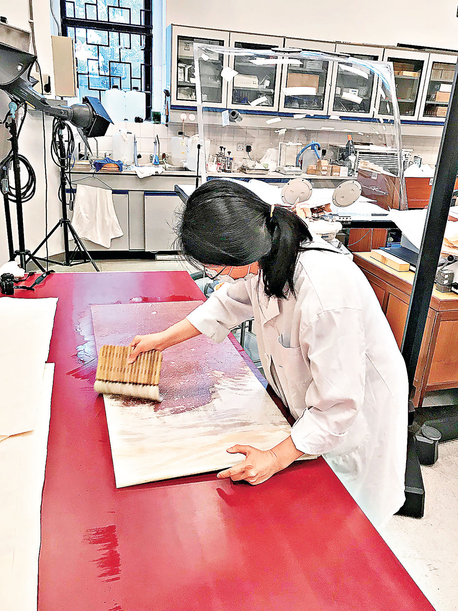 ■文物修復師在漆枱上用排掃將紙張濕水刷平。 康文署提供