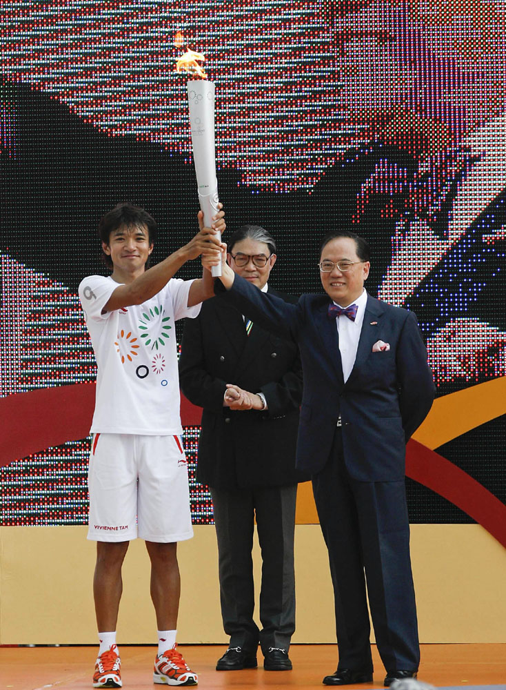 　　圖：第一棒火炬手黃金寶（左）在曾蔭權手中（右）接過火炬（新華社）