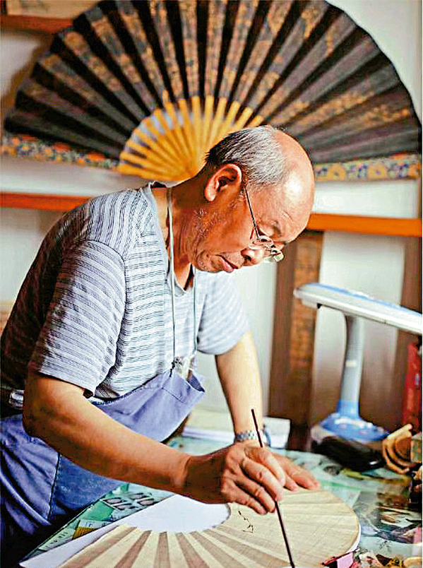 　　圖：陳子福在扇面上繪畫