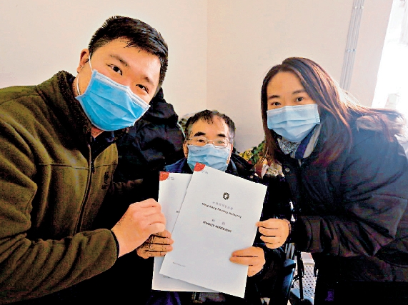 　　圖：黃伯（中）手持與房署簽訂的新租約，終於放下心頭大石。/大公報記者方學明攝