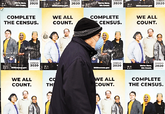 　　圖：去年4月，一名戴着口罩的男子經過西雅圖街頭宣傳人口普查的海報。\美聯社