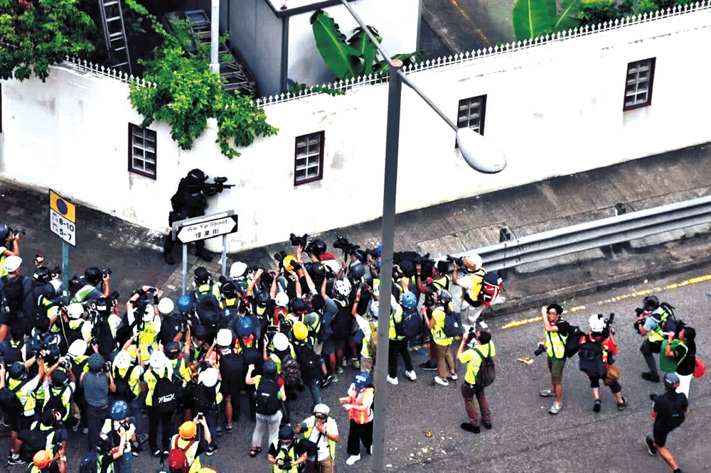 　　圖：黑暴期間假記者充斥暴亂現場，前年觀塘一場暴亂中有警員持槍戒備，現場數十人圍着警員，掩護暴徒。