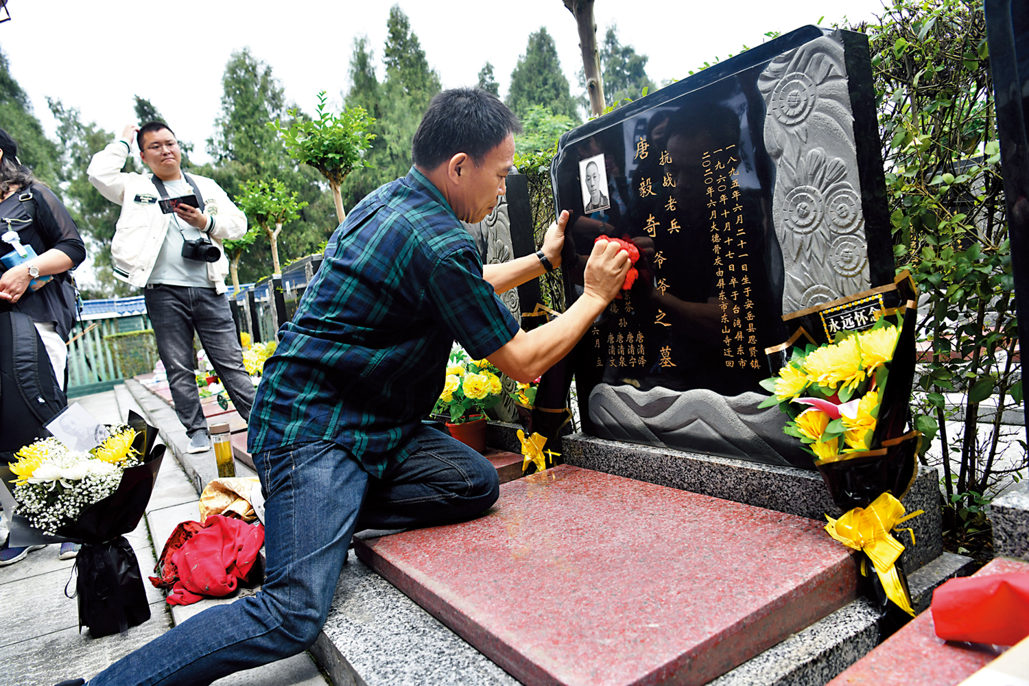　　圖：18日在四川省資陽市安岳縣岳陽公墓，台胞劉德文將台灣老兵唐毅奇的骨灰罎安葬在墓穴內後，用布擦拭墓碑。\中新社
