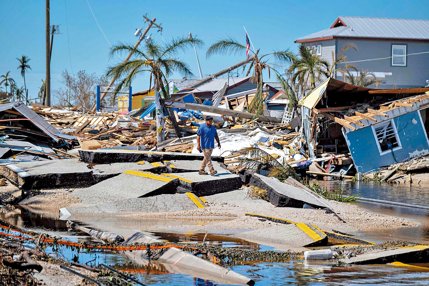 　　圖：自然災害重創美國經濟。10月，佛羅里達州經歷一場颶風後，一名男子走過滿目瘡痍的路段。