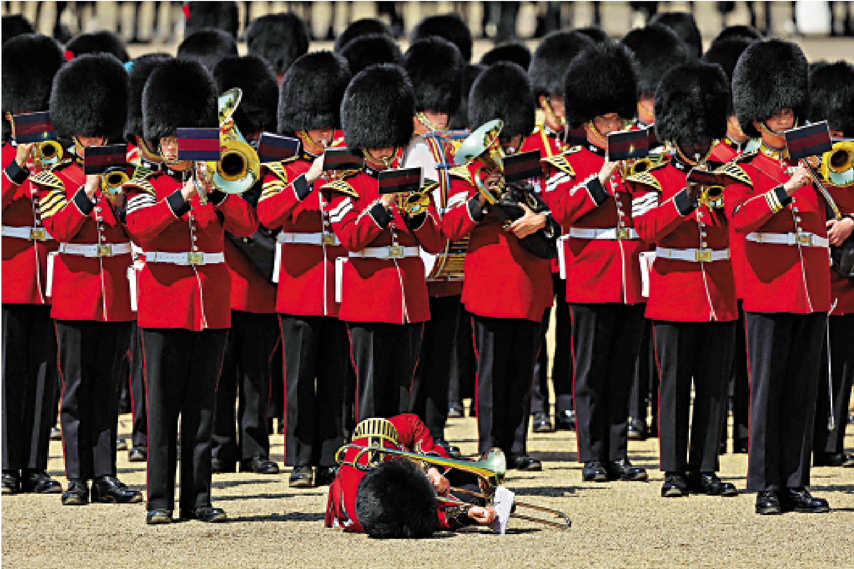 　　圖：去年6月，一名戴着熊皮帽的英國皇家衛隊士兵在君主壽辰軍禮的綵排中被熱暈倒地。\法新社