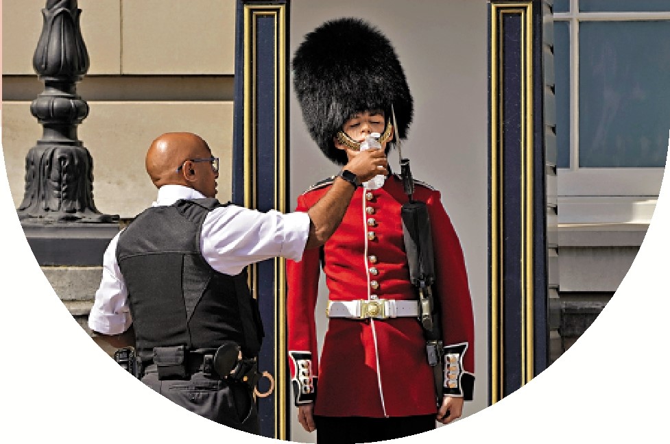 　　圖：2022年7月，一名警察給戴着熊皮帽的衛兵餵水喝。\美聯社