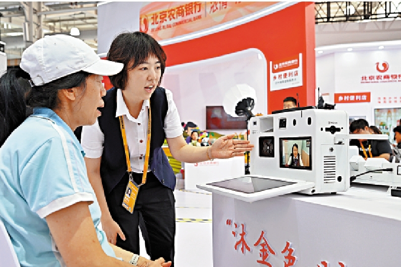 　　圖：去年在北京舉辦的服貿會上，北京農商銀行展台工作人員向參觀者介紹一款自主設計的視頻銀行。/新華社