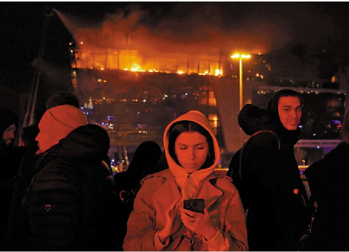 　　圖：俄羅斯民眾在起火的音樂廳外用手機查看消息。/法新社