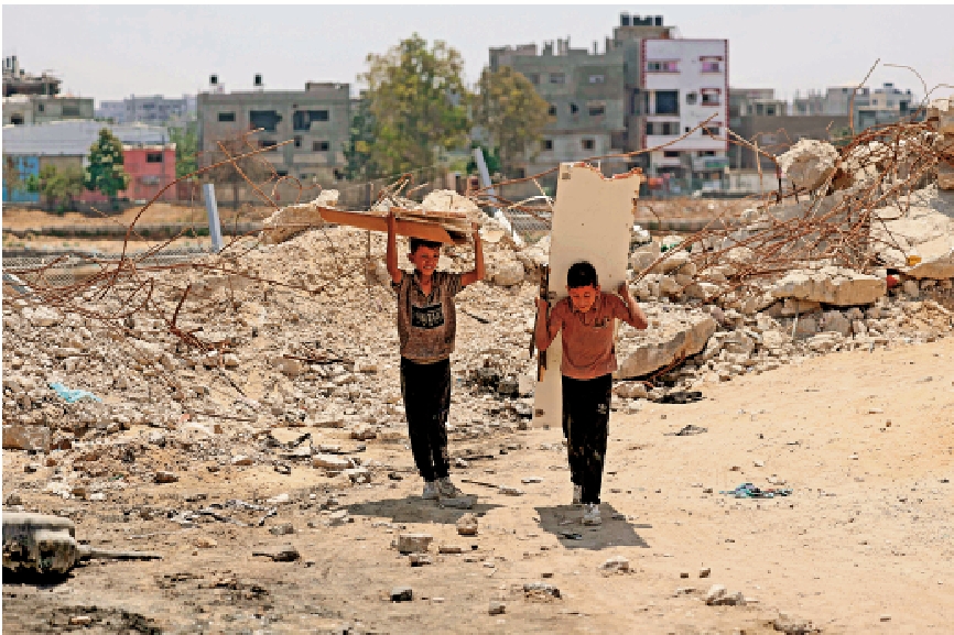 　　圖：背着木板的加沙兒童經過遭以軍炸成廢墟的建築。\法新社