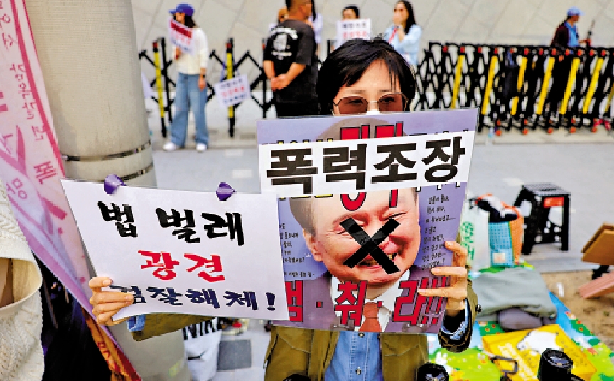 圖:一名民眾11日在尹錫悅私人住所附近高舉標語,指責尹錫悅「推行暴力」。\路透社