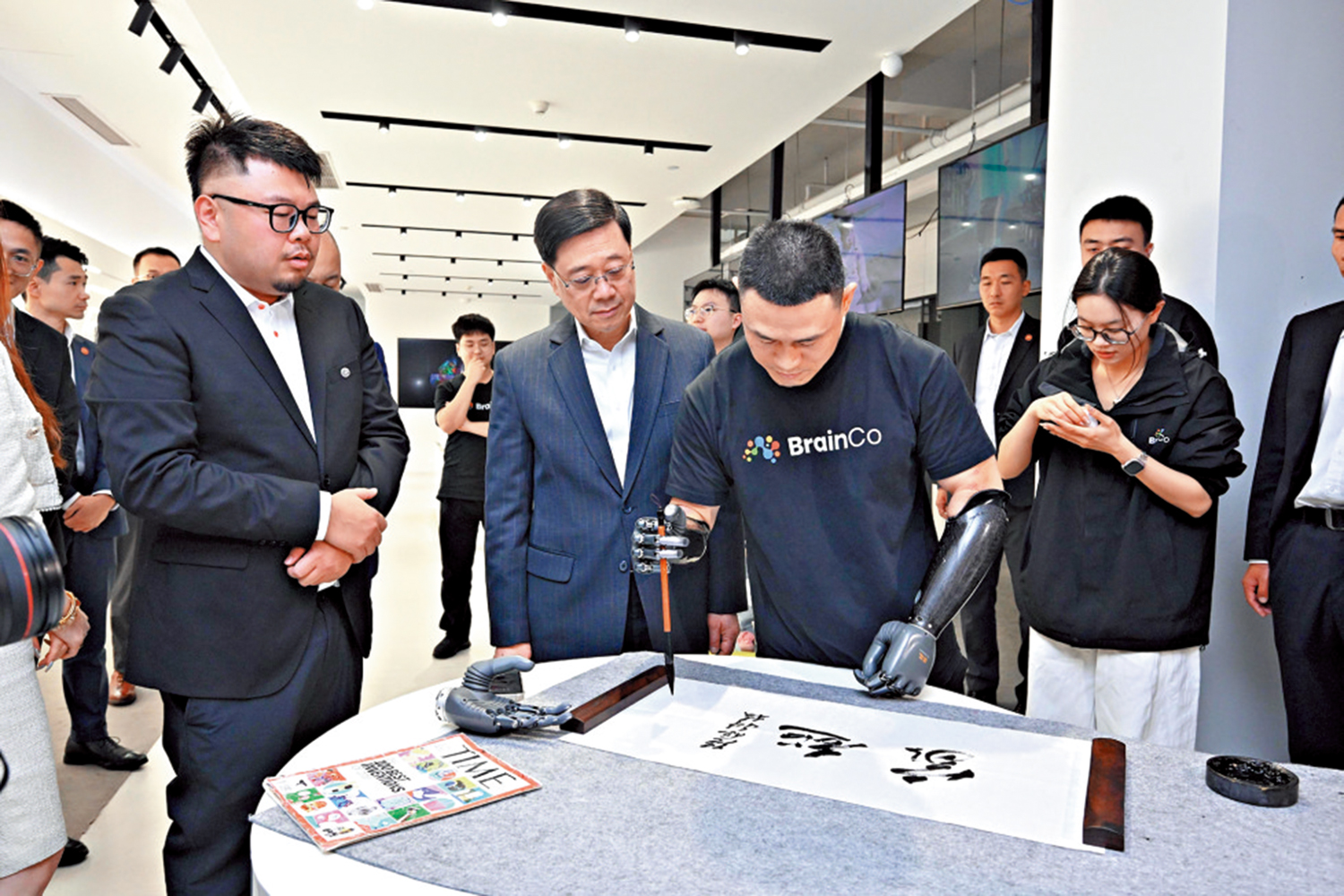 圖:李家超參訪強腦科技,職員展示如何用智能義肢寫書法。