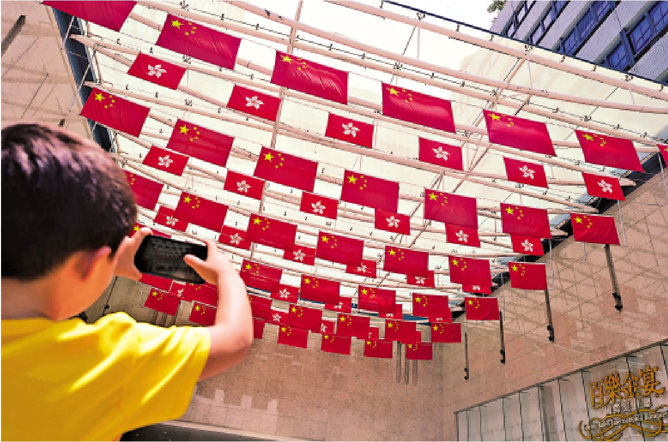 　　圖：七一將至，全港多區掛起國旗與區旗，吸引小朋友拍照紀錄。\大公報記者蔡文豪攝