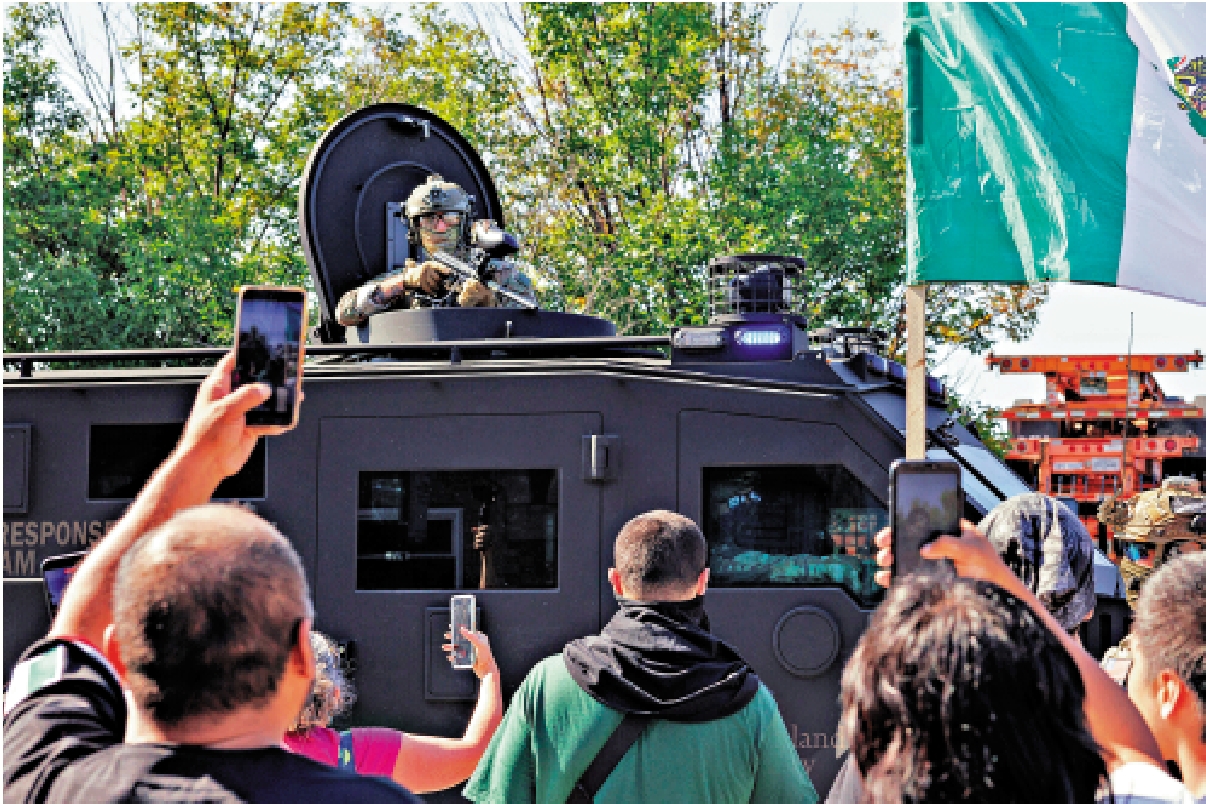 　　圖：一名移民執法人員4日在芝加哥用槍指着示威者。\美聯社