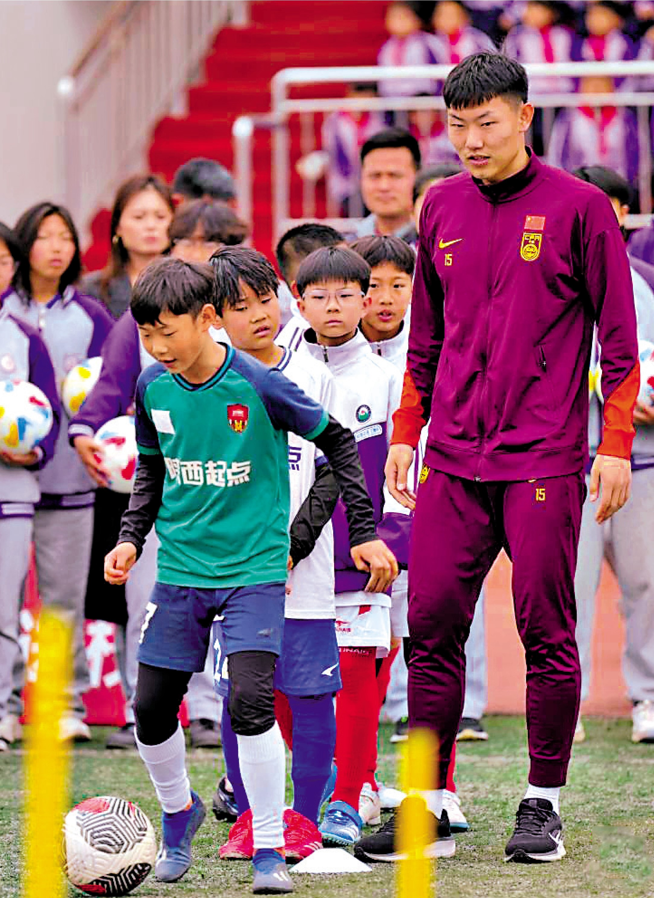 　　圖：U23國足球員史松宸（右）指導小球員踢足球。\新華社