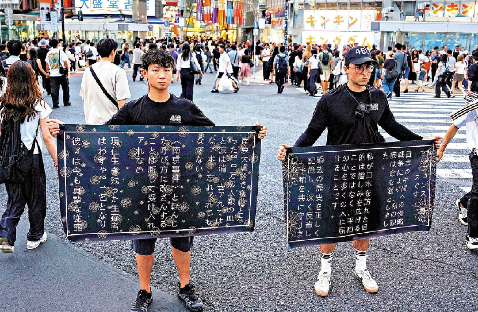 　　圖：在東京澀谷街頭，法國青年馬庫斯‧德雷特斯（右）和友人鍾灝松舉起橫幅，呼籲日本社會正視對外侵略歷史。\新華社