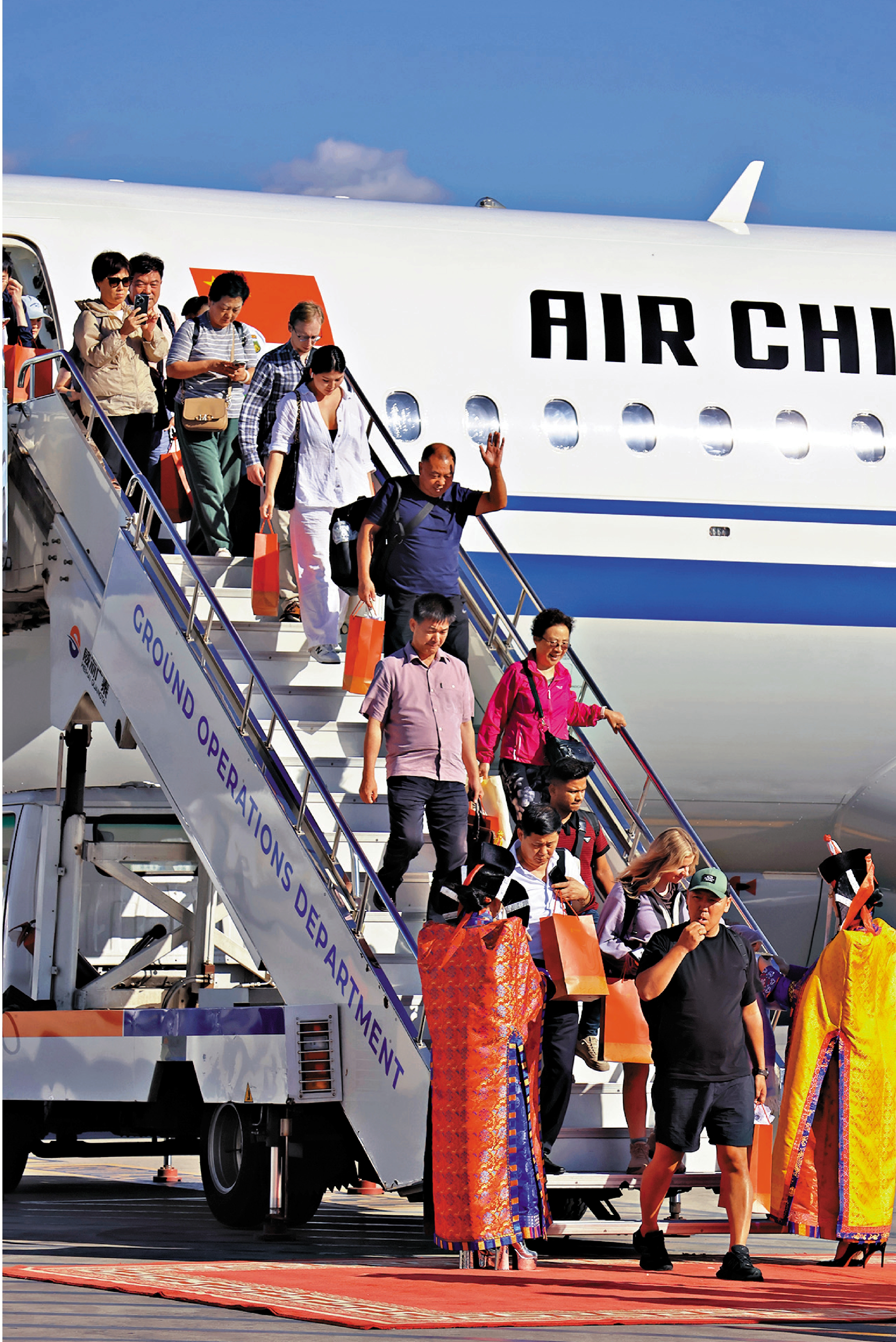 　　圖：8月12日，在蒙古國新烏蘭巴托機場，旅客在身着蒙古國傳統服飾的禮儀人員迎接下走出機艙。/新華社
