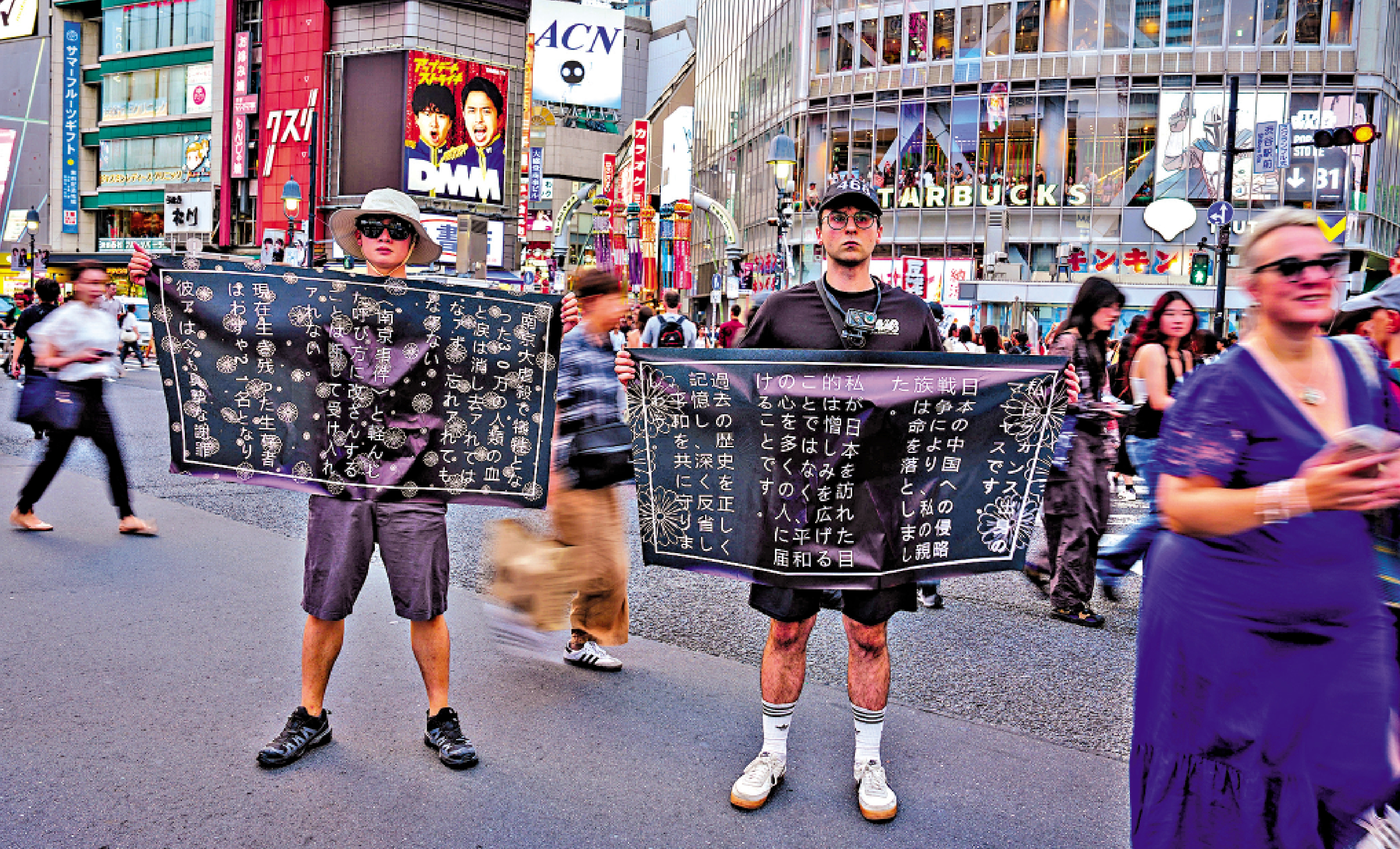 　　圖：8月5日，在東京澀谷街頭，法國青年馬庫斯·德雷特斯（右）和友人鍾灝松手舉橫幅，呼籲日本社會正視對外侵略歷史。\新華社