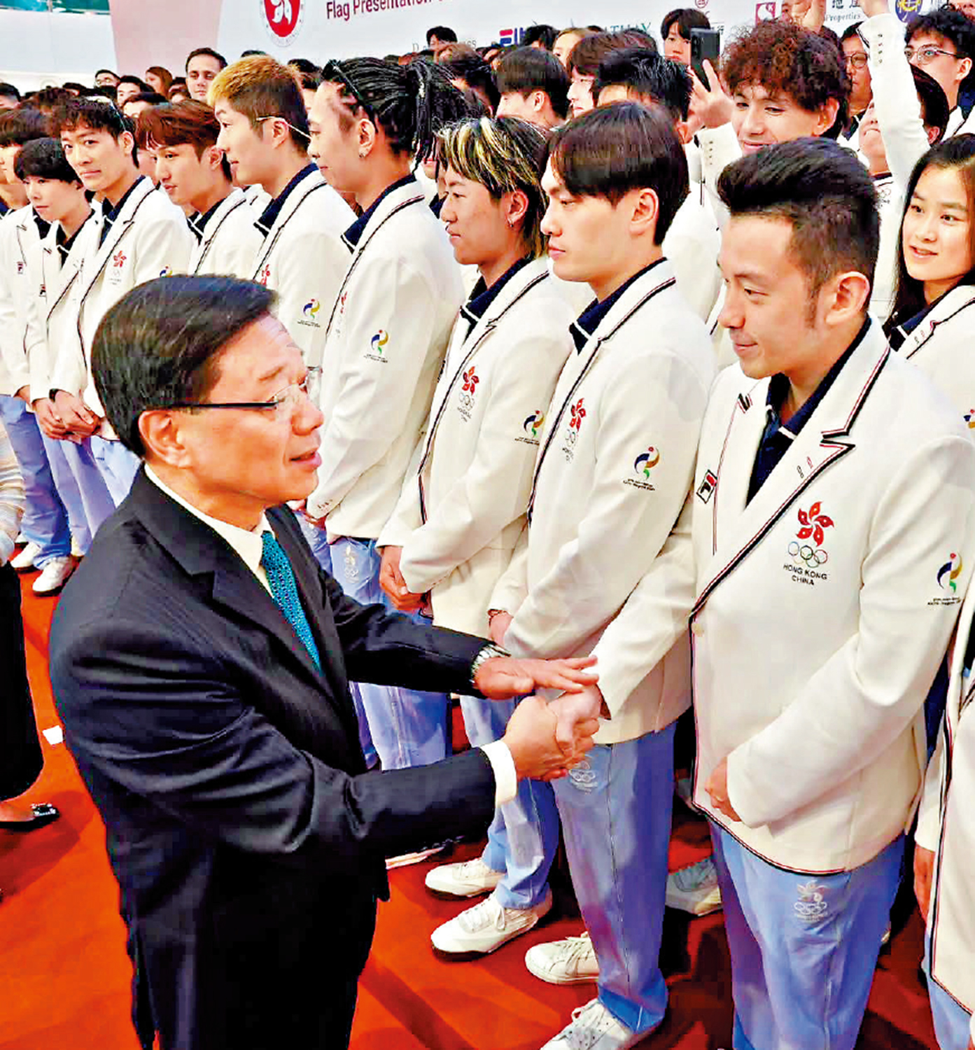 　　圖：李家超（左）在亞運中國香港代表團授旗禮上，與乒乓球運動員黃鎮廷握手。\資料圖片