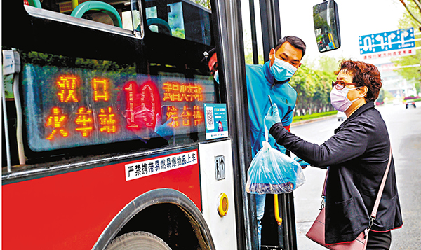 實名登記  ■武漢部分公交線路昨日恢復運營，圖為一名公交安全員指導乘客用手機掃碼實名登記上車。  中新社