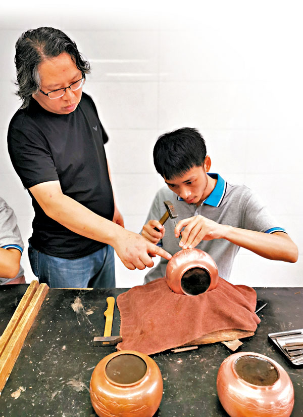 ■黃俊軍（左）在指導兒子黃寬進行金屬鏨刻。香港文匯報記者王逍  攝