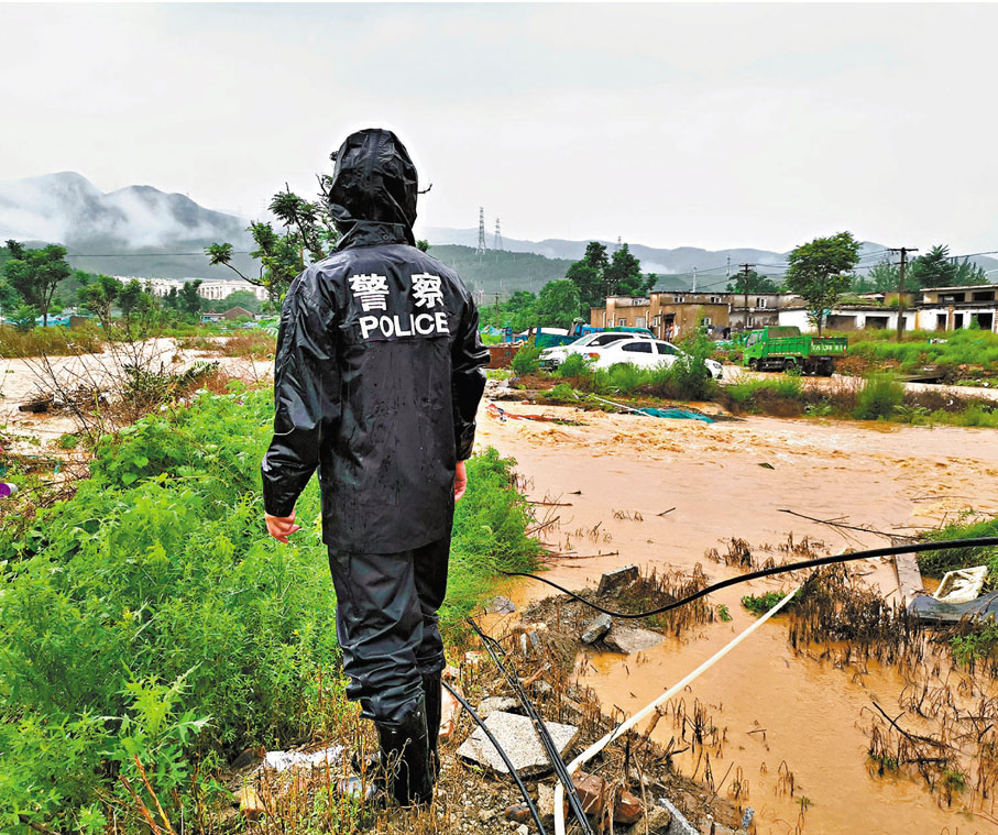 ●7月18日，北京門頭溝區，一名警察在檢查被暴雨引發的洪水毀壞的道路。 新華社