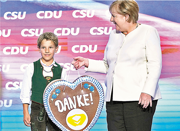●默克爾（右）日前在基民盟選舉集會上，獲贈寫上感謝的紀念品。 美聯社