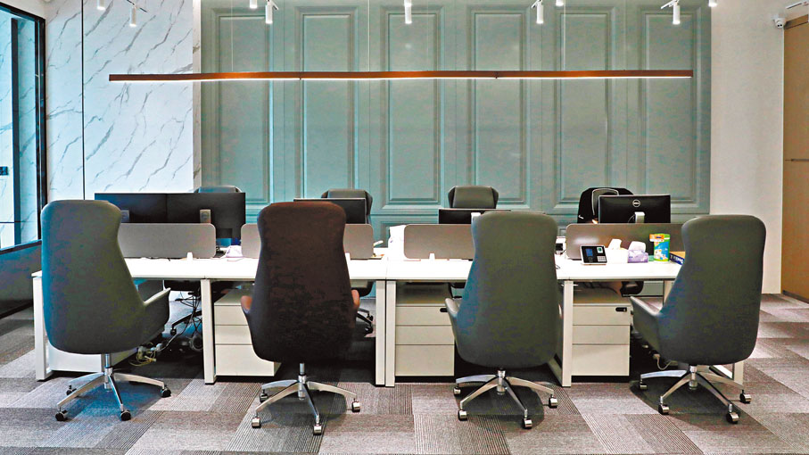 ●在辦公室區域，白色的桌子搭配灰色的皮凳，牆身用英式設計的灰綠色花線牆。