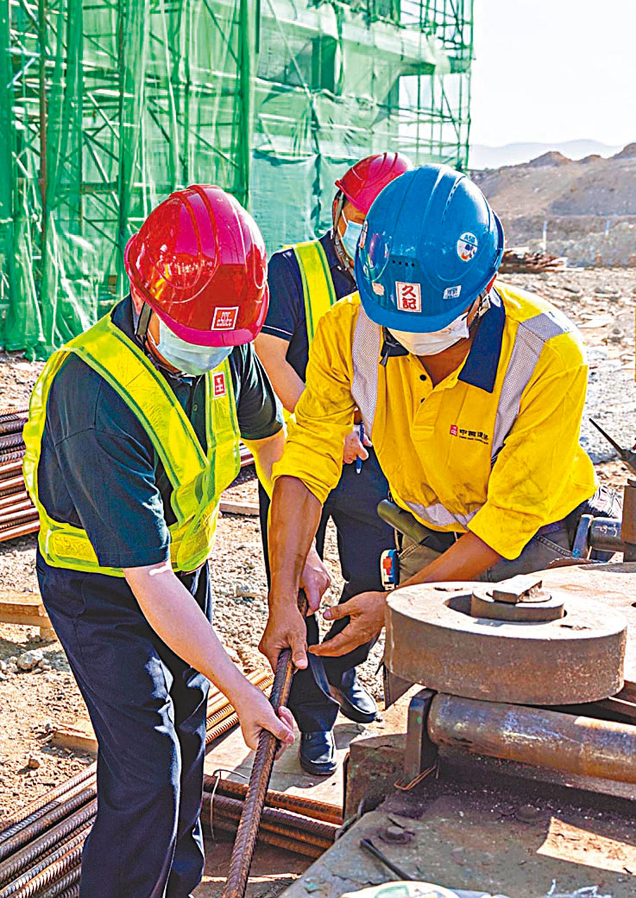 ●譚鐵牛副主任（左）在地盤施工現場向工友學習紮鐵。中聯辦網站圖片