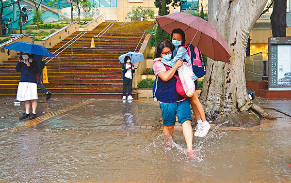 ●在銅鑼灣中央圖書館附近，家長抱起女兒走過積水路段。  香港文匯報記者  攝