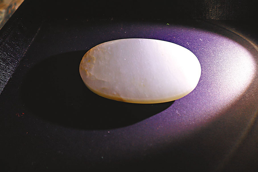 ●鵝蛋形素面帶扣，用電筒照玉器時可見明顯的白花紋。