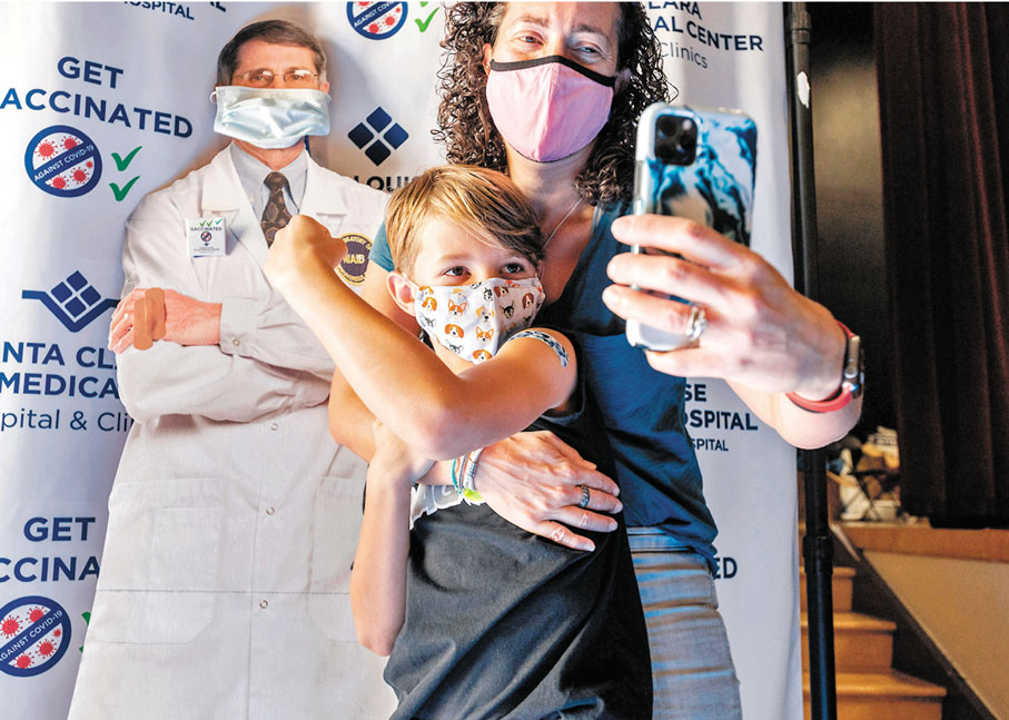 ● 美國9歲男童接種後站在福奇肖像前與母親拍照。 美聯社