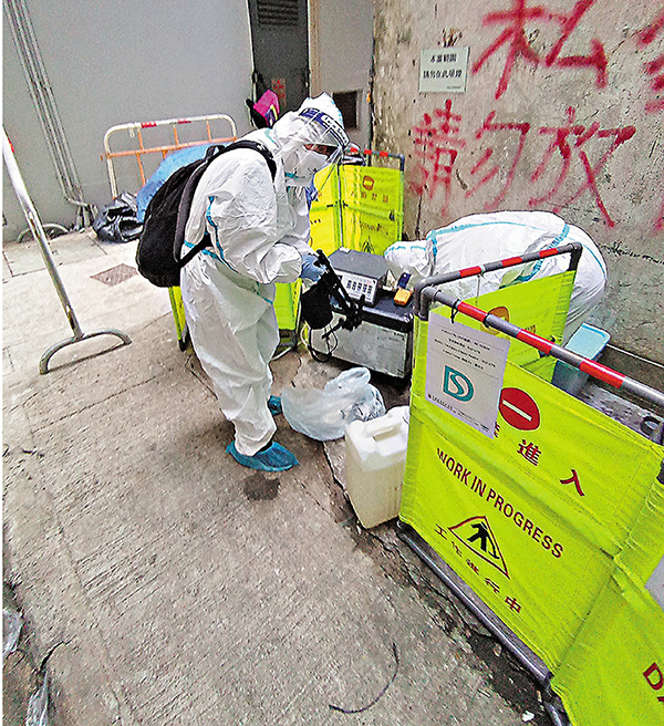 ◆ 身穿全套保護裝備的工作人員打開大廈後巷地面渠蓋進行污水採樣工作。圖：香港文匯報記者  攝