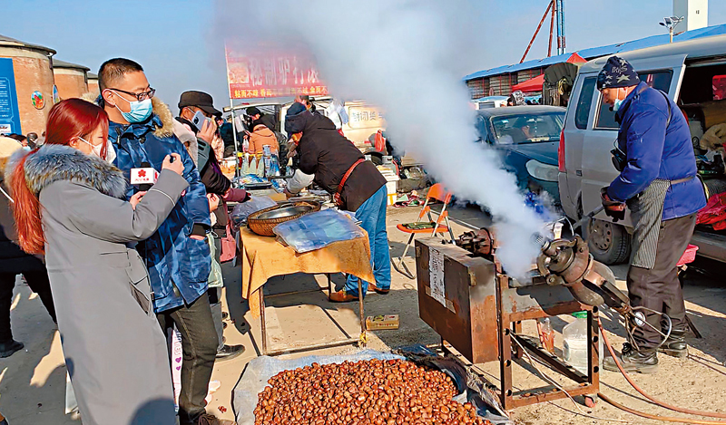 ◆林競秀（左一）圍觀傳統東北小吃「崩栗子」的製作。