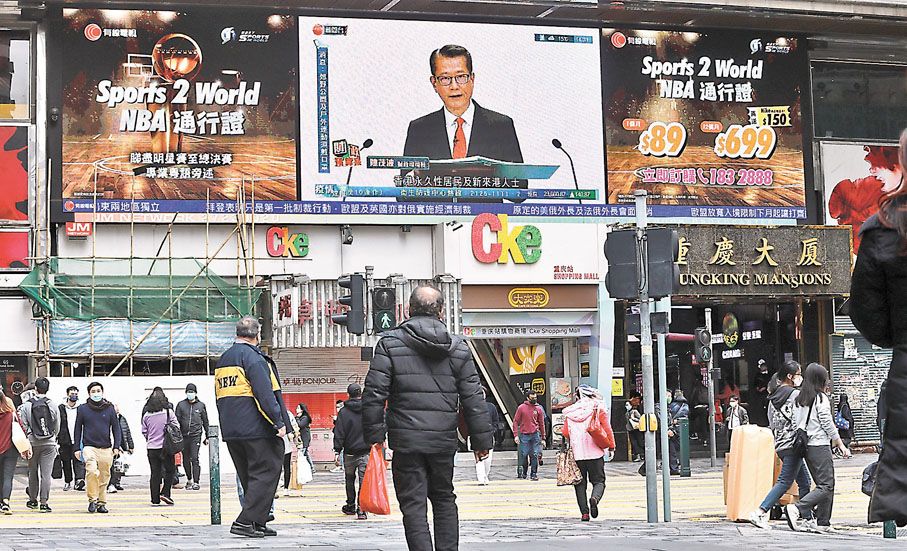 ◆陳茂波表示，因應抗擊第五波疫情開支及預算案再度派發1萬元消費券的措施，估計本年度會出現財政赤字。圖為市民在街頭觀看財案直播。香港文匯報記者  攝