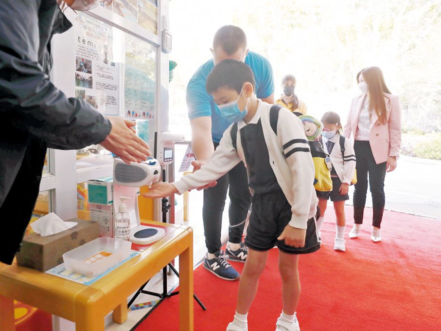 ◆幼稚園復課,老師在門口指示學生消毒鞋底及雙手。香港文匯報記者 攝