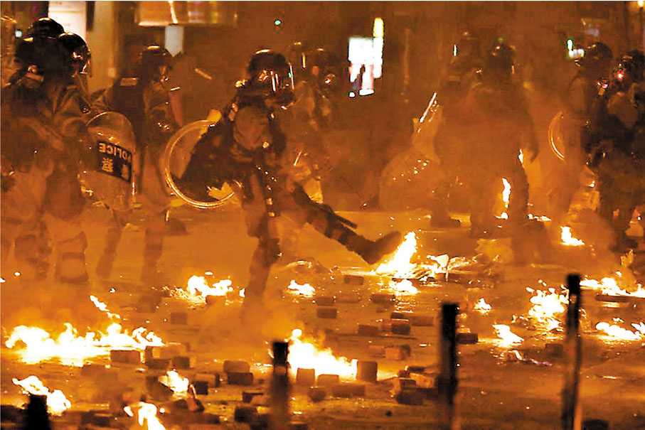 2019年11月18日晚黑暴在理大外圍「火攻」警方防線，下圖為防暴警冒着地面火勢驅散暴徒。 資料圖片