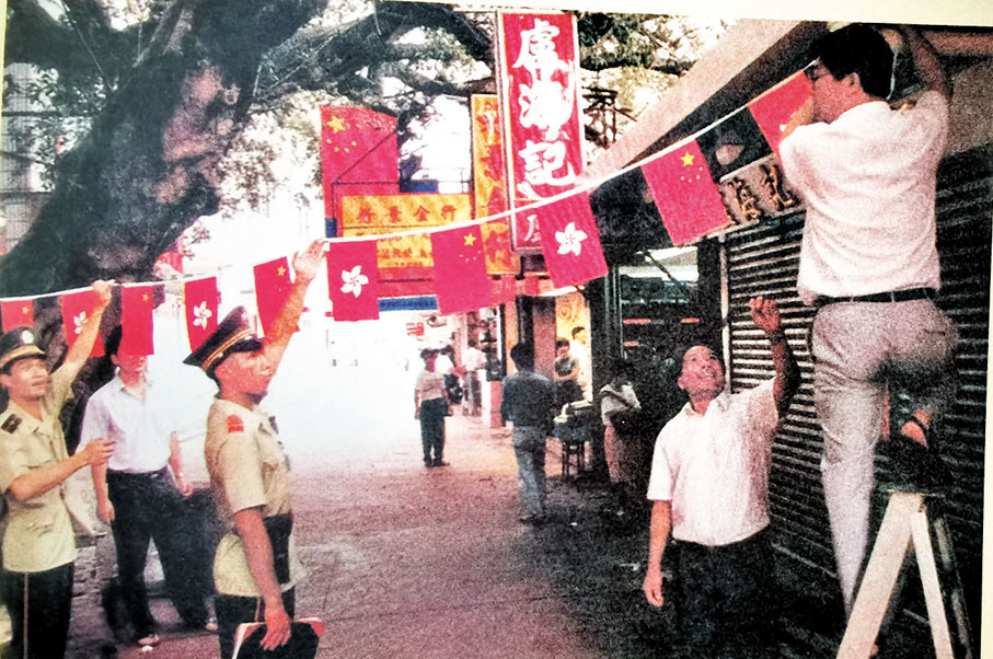 ◆香港回歸前夕，「沙頭角模範中隊」的戰士和深港兩地居民在中英街懸掛國旗和區旗。香港文匯報記者郭若溪 翻拍