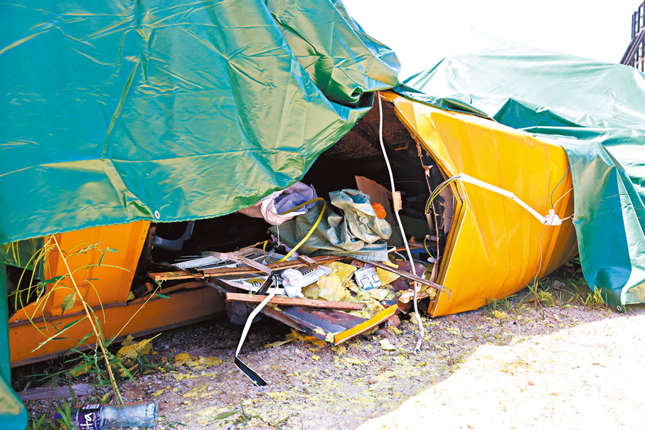 ◆其中一個遭天秤壓扁的貨櫃辦公室被吊到路邊用帆布掩蓋。香港文匯報記者  攝