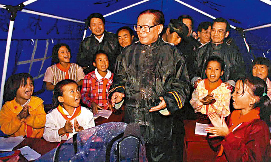 ◆1998年9月4日，江澤民冒雨在江西省九江察看災情，指導抗洪救災工作。 圖為江澤民在臨時教學點的帳篷裏看望小學生。 資料圖片
