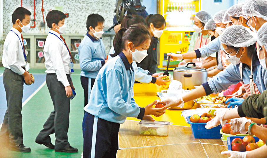 ◆小學生排隊拿取師生家長自己下廚的午餐。香港文匯報記者郭木又  攝