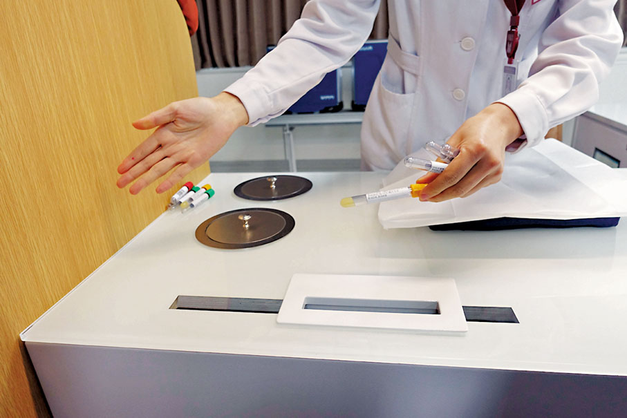 ◆ 一名護士為患者抽血，其抽血樣本可放入桌面上的標本運輸管道，60秒無縫轉運到檢驗科。 香港文匯報記者盧靜怡  攝
