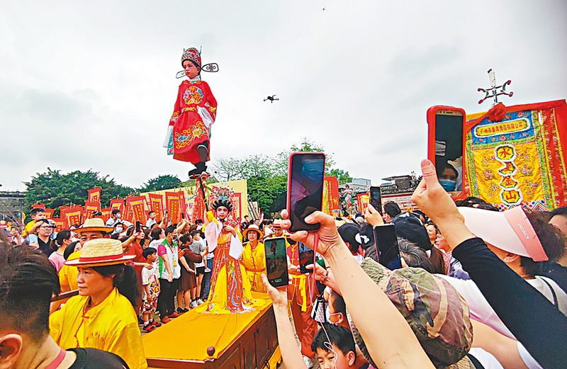◆身着華麗戲服的小孩高高「懸」在空中，巧妙地單腿獨立在一根竹枝上，引來路上市民紛紛拍照。