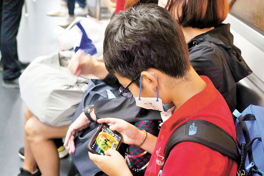 ◆調查發現31.8%受訪中小學生曾連續打機5小時或以上,最年幼者僅6歲至8歲。圖為青年在港鐵玩手遊。 資料圖片