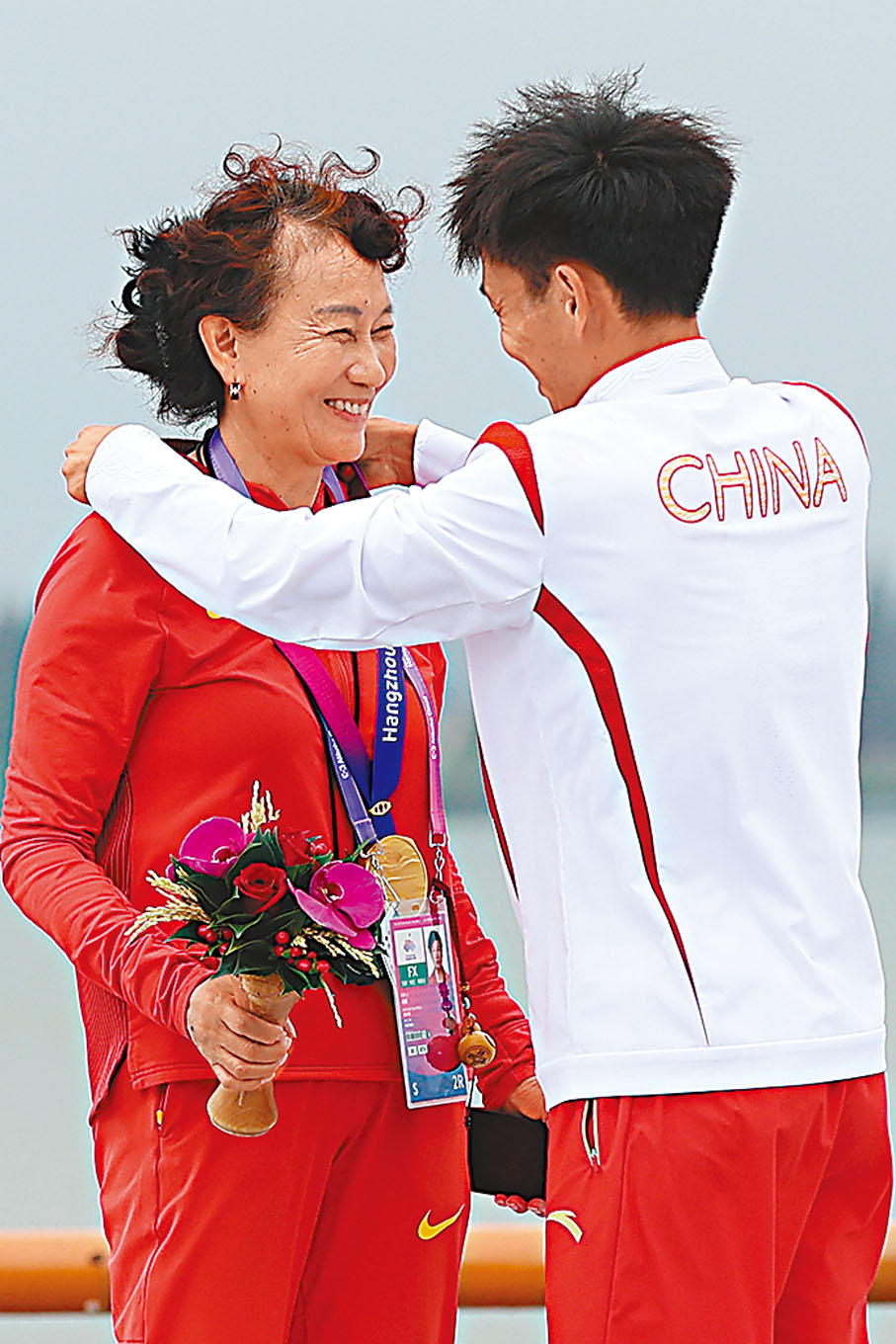 ◆何傑邀請教練肖麗（左）登上領獎台，並將金牌掛在她身上。  中新社