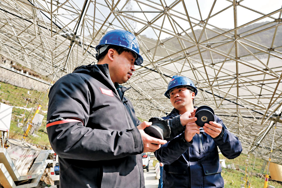 ◆姜鵬（左）在貴州「中國天眼」的反射面板下與工作人員交談。 網上圖片