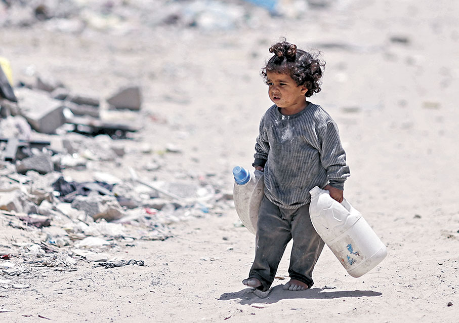 ◆一名巴勒斯坦孩童拿着罐子走過被毀房屋。   路透社