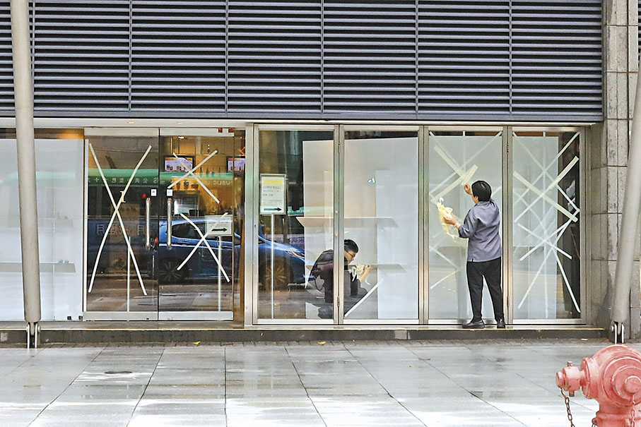 ◆天文台改發三號強風信號後，有店舖職員忙於清理貼在玻璃上的防風膠紙。 香港文匯報記者北山彥 攝
