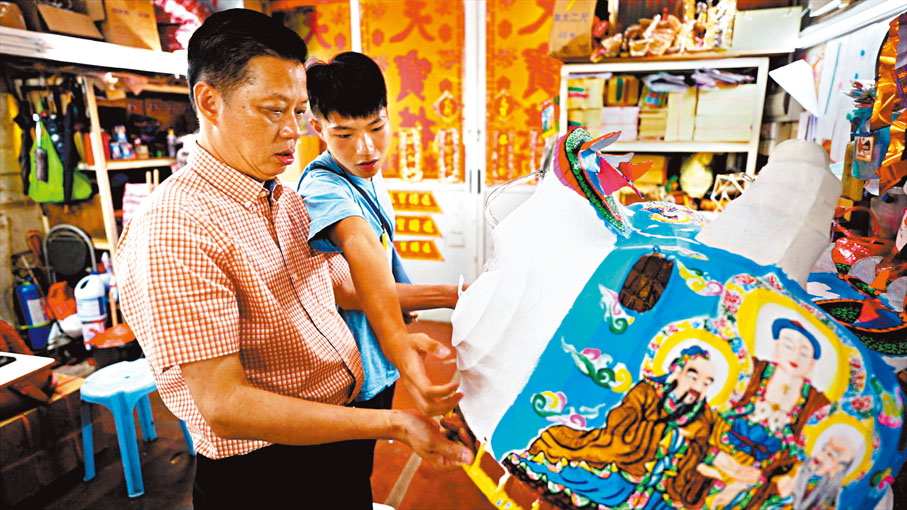 ●年僅17歲伍彥維（右）為是次國慶展覽製作了「三教獅頭」，左為其師父夏中建。 受訪者供圖